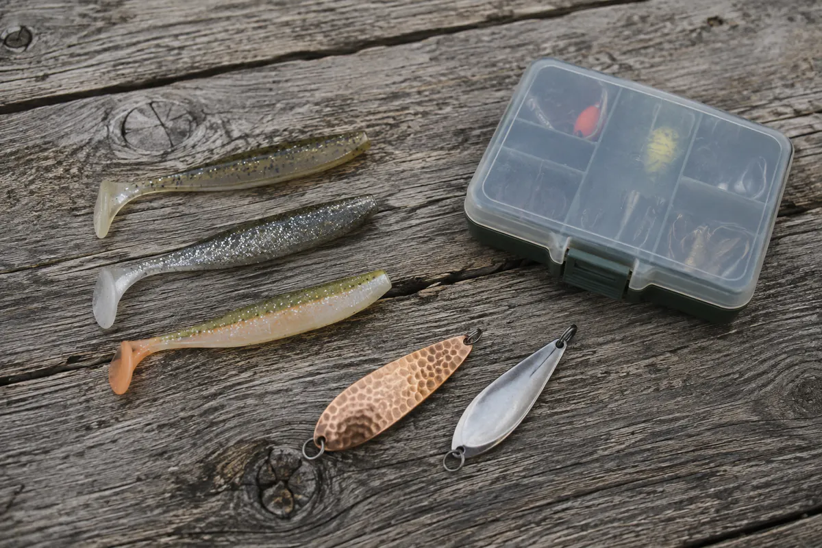 Gummifische, zwei Blinker und eine Köderbox auf Holz